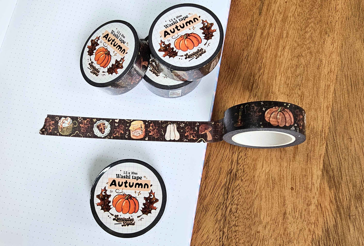 Three rolls of decorative washi tape with an autumn theme are displayed on a white dotted notebook and a wooden surface. The tape features illustrations of pumpkins, acorns, leaves, and the text 'It's Fall, So I'm Washi Tapes Autumn'.