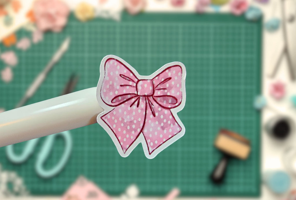 Pink bow with white polka dots on a pen against a green cutting mat background