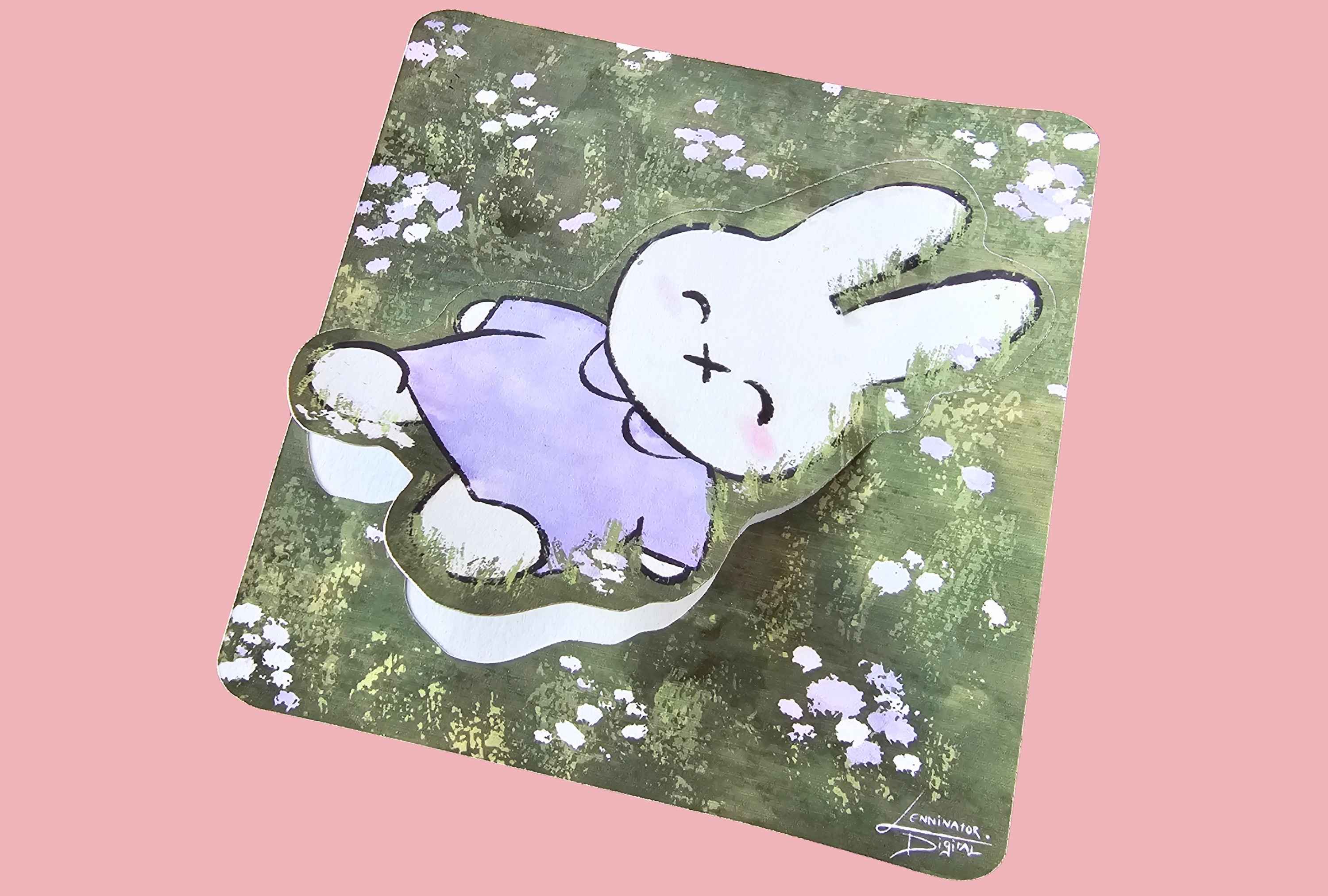 A square mousepad with rounded corners featuring a cartoon rabbit illustration, shown at an angle against a solid pink background. The mousepad has a green and brown textured background with small white flowers, and the rabbit is white with a purple shirt.