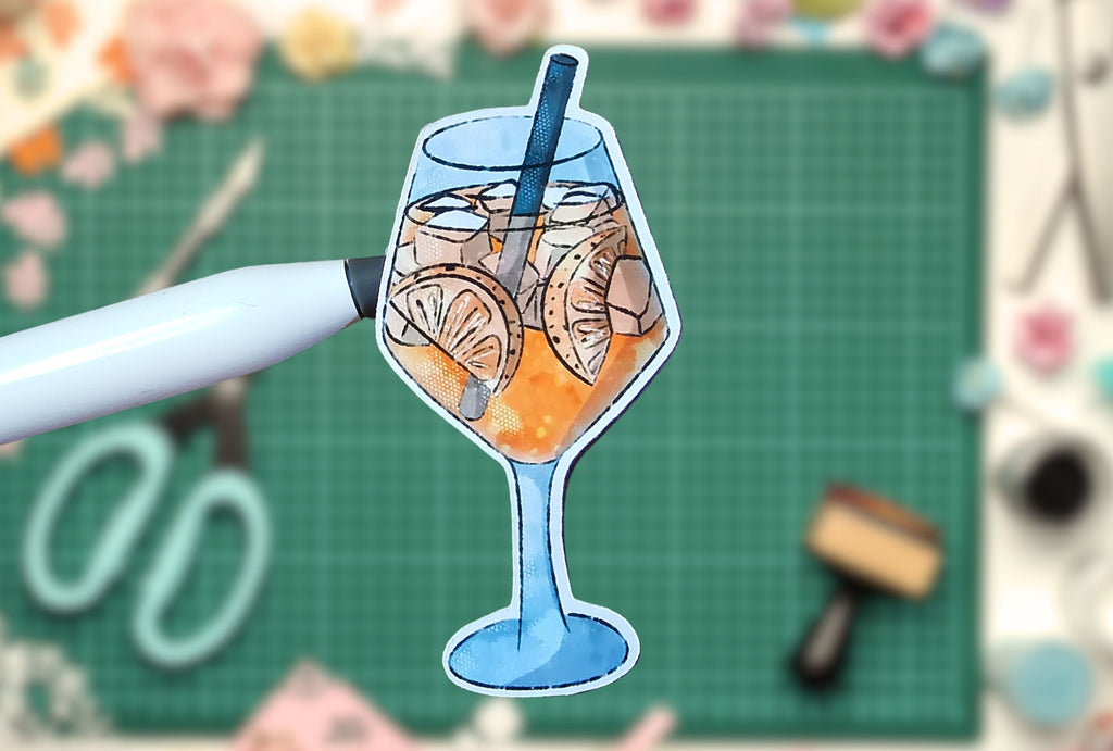 Sticker of a Aperol Spritz cocktail glass with ice and orange slices on a cutting mat with tools.