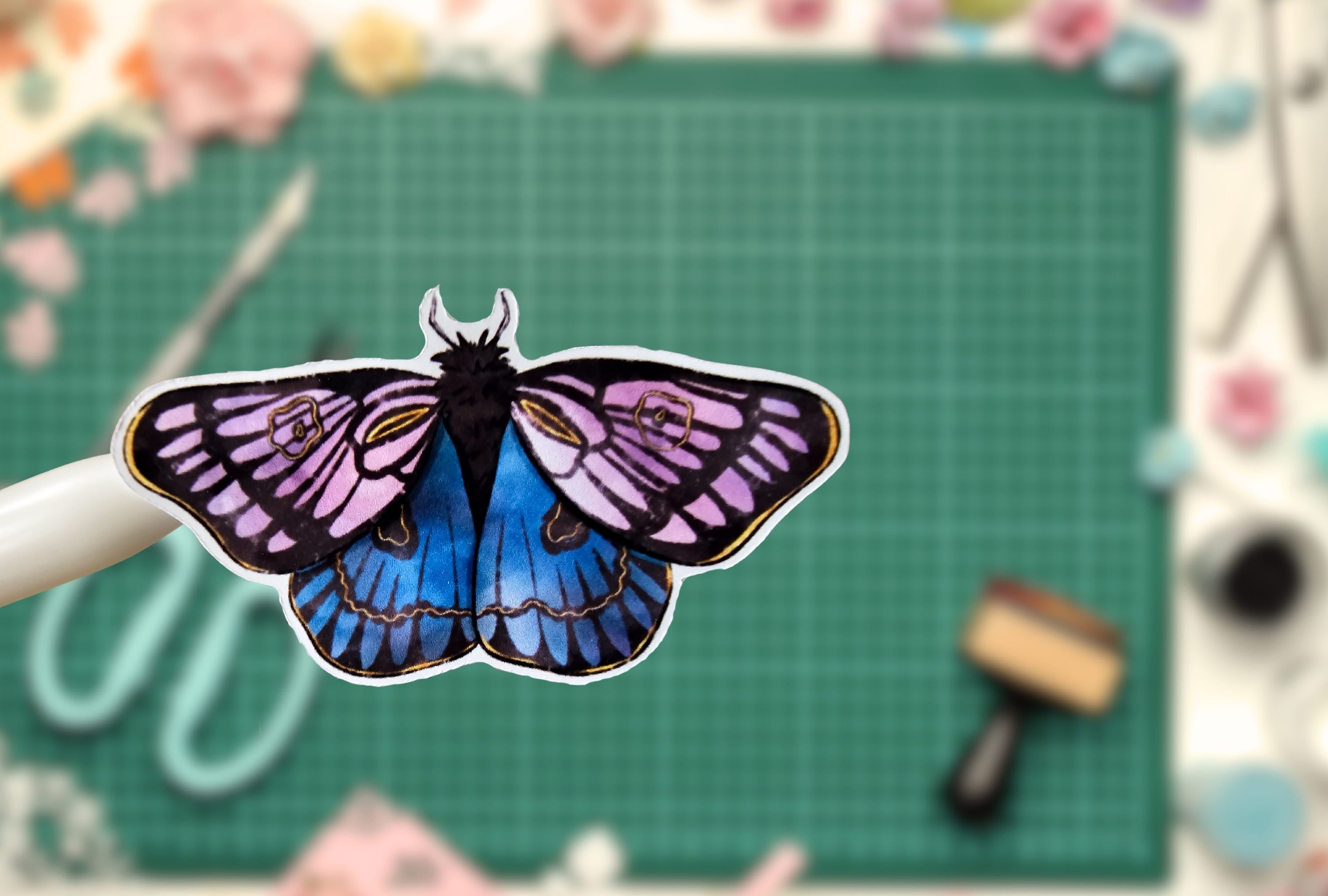 Butterfly-shaped sticker on a green cutting mat with crafting tools in the background