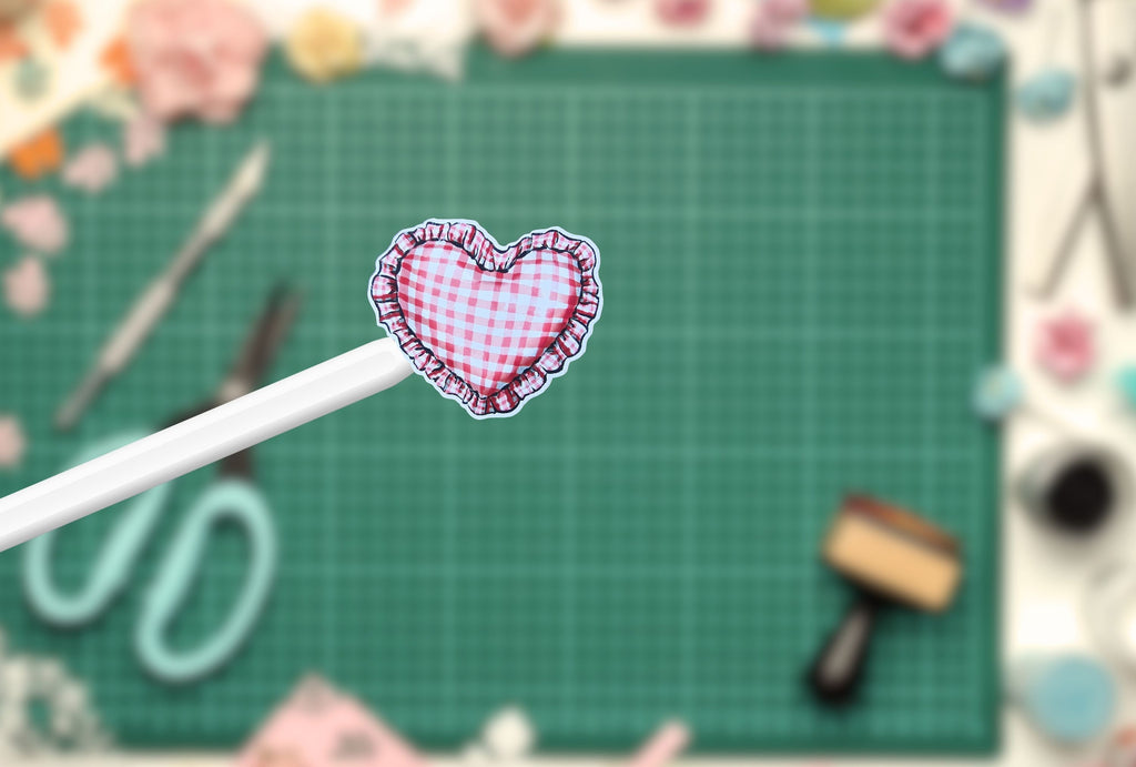 Heart-shaped gingham sticker on a pen with a green cutting mat and craft tools in the background