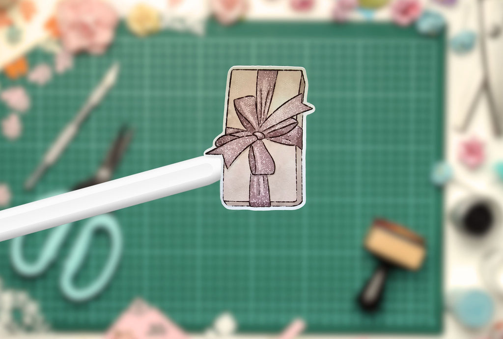 Decorative gift sticker with a bow design on a green cutting mat with tools in the background.