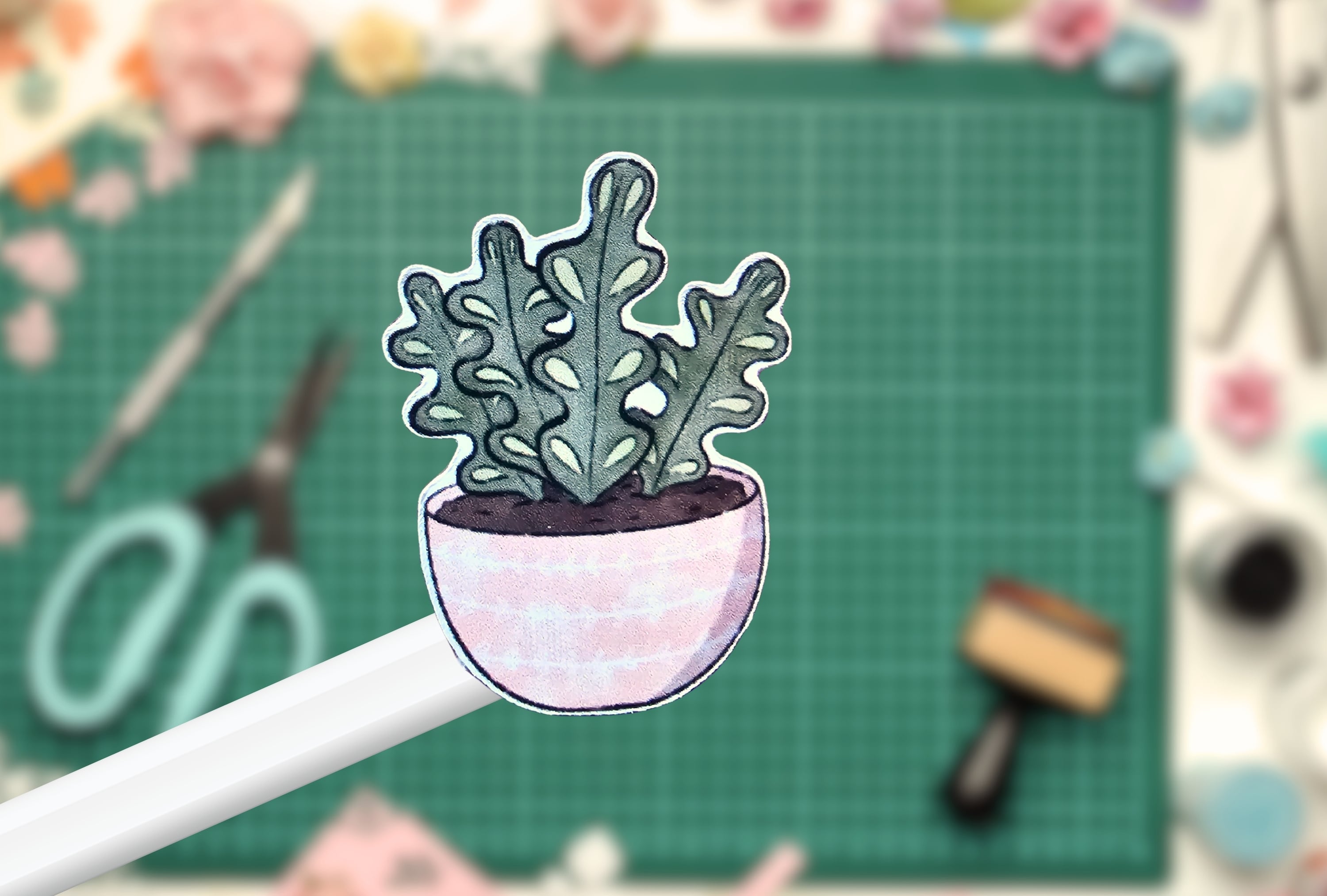 Cute plant on a white pen against a green cutting mat with tools in the background