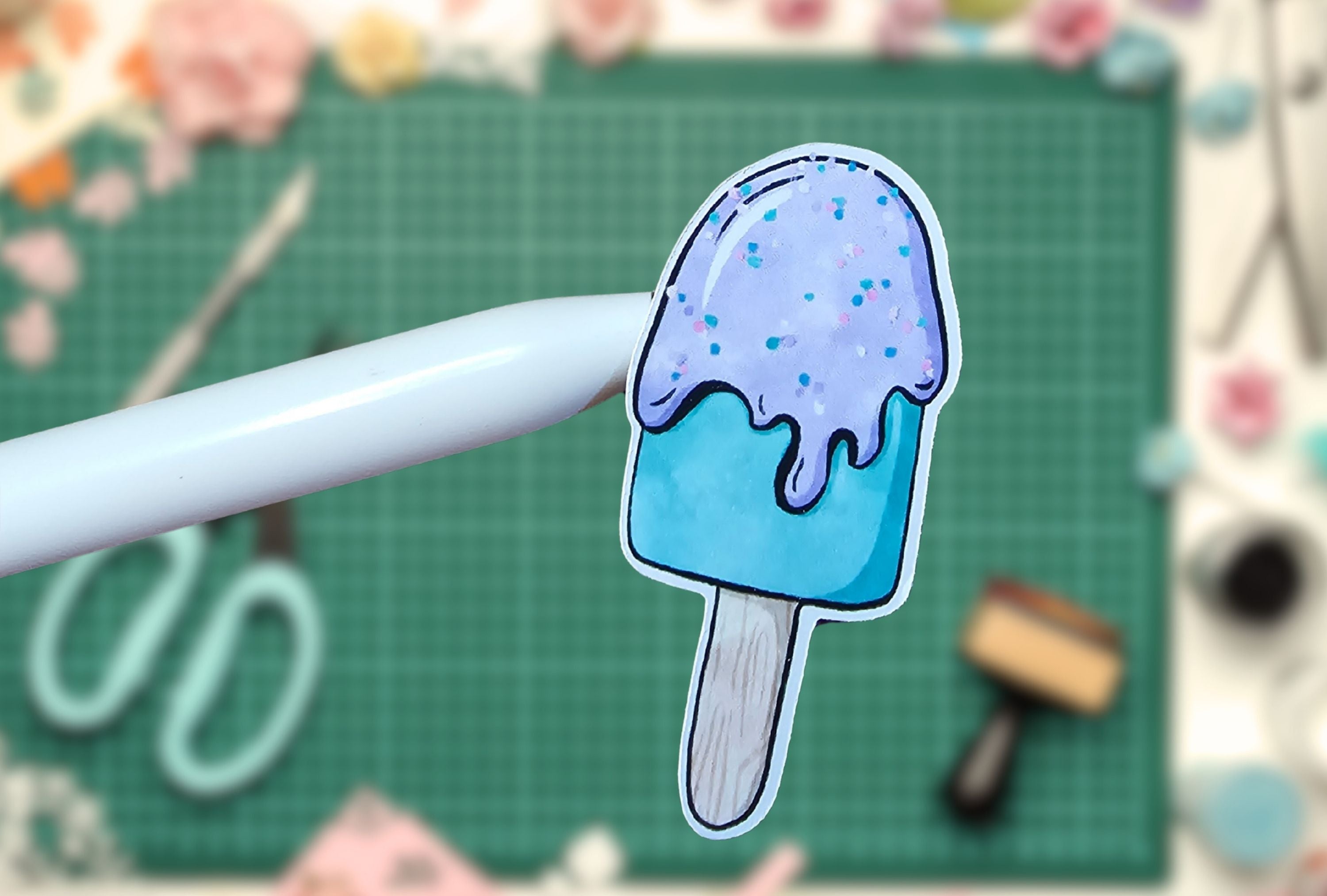 Blue ice cream popsicle sticker on a white pen with a green cutting mat background