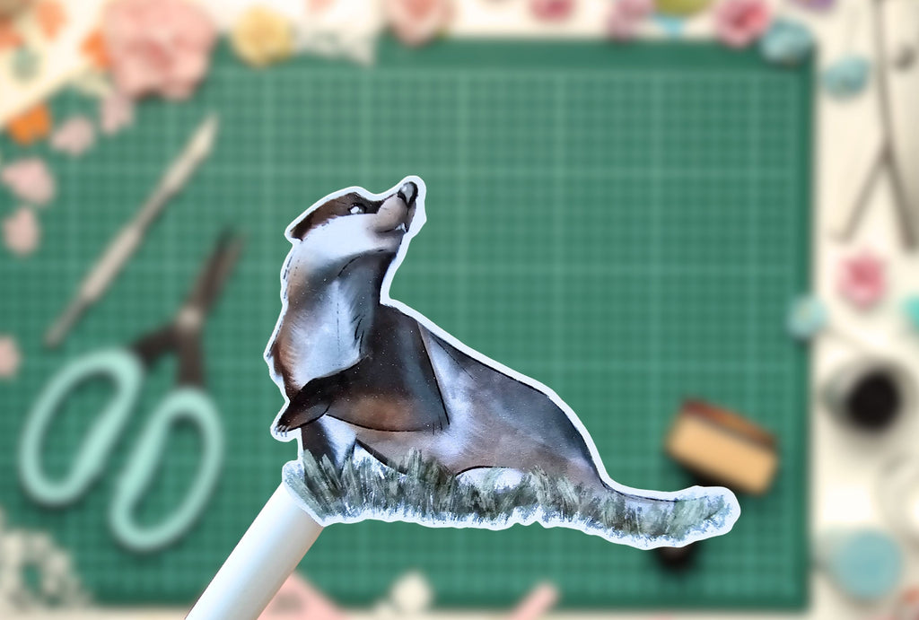 Sticker of a badger on a pencil with a green cutting mat and scissors in the background