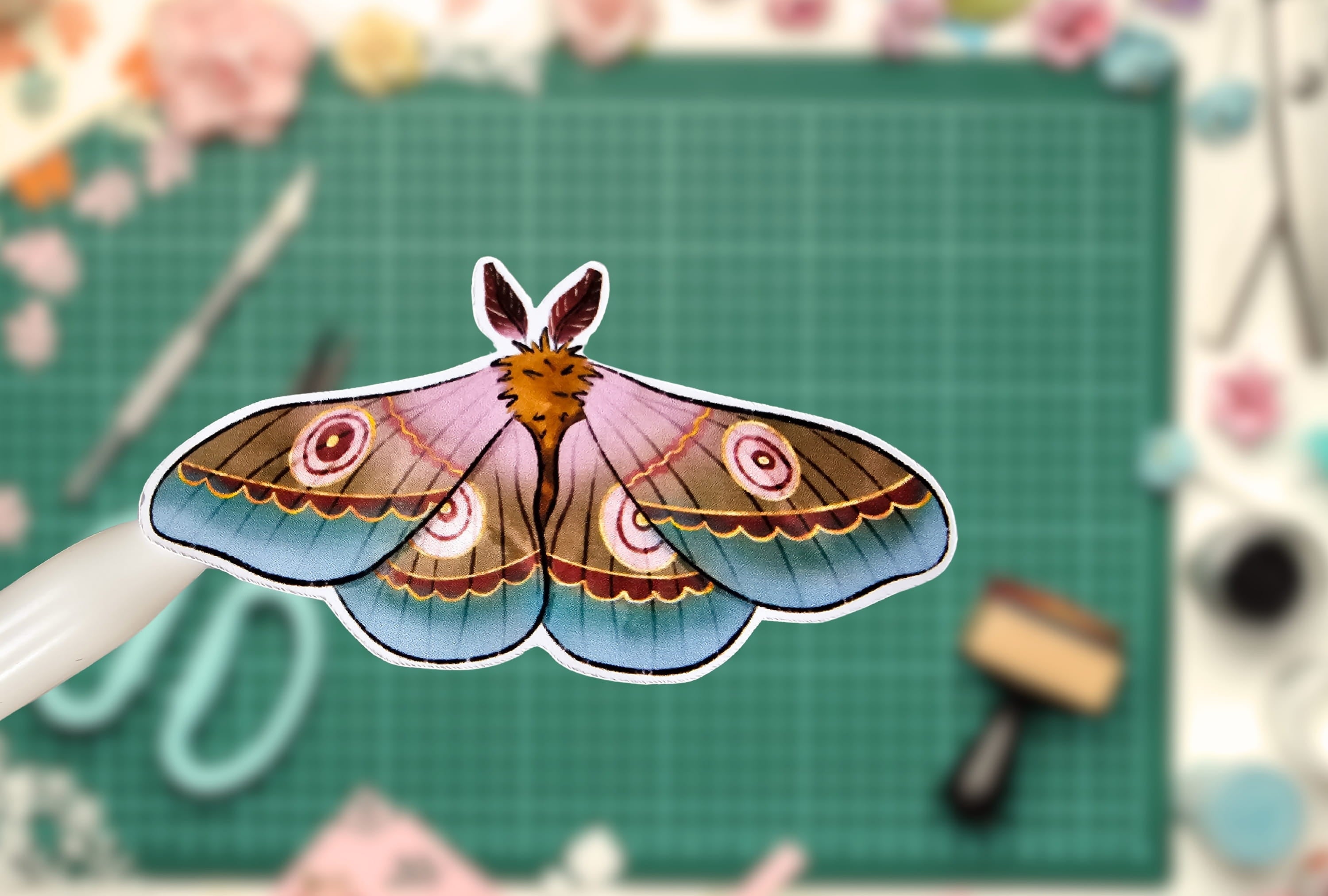 Colorful butterfly design on a green cutting mat with crafting tools.