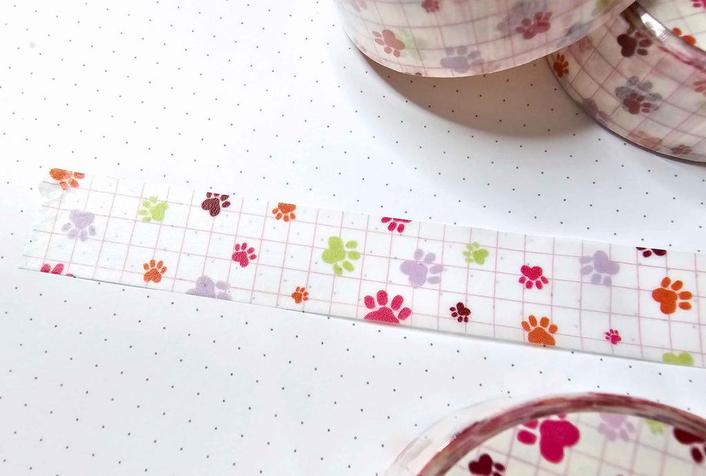 close up of a pet paw washi tape with scatered pet paws in various colors on a white background with pink grid