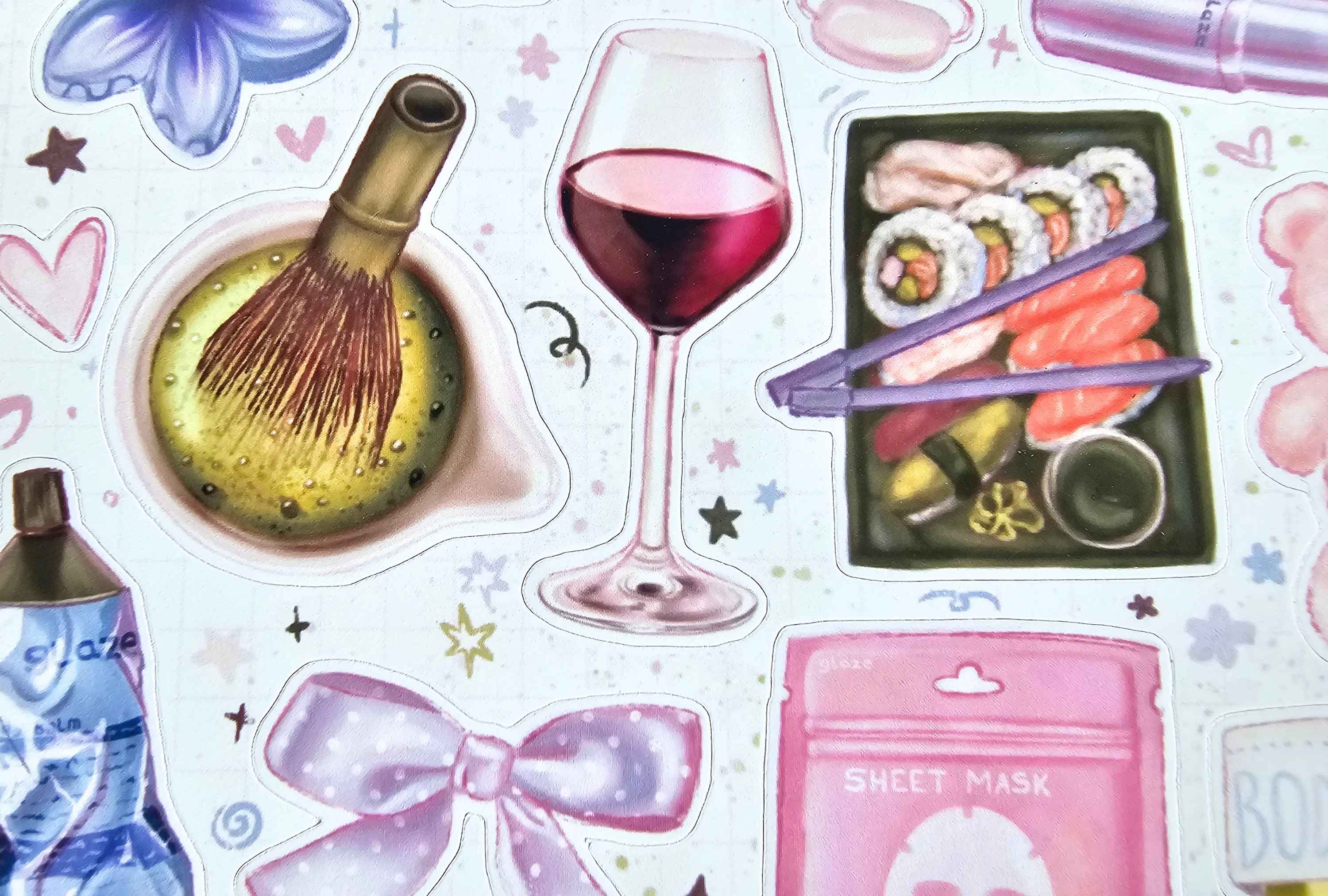 A close-up of a sheet of decorative stickers featuring pastel illustrations of a wine glass, sushi, a pink bow, a sheet mask pouch, and other food and beauty-themed motifs on a light background.