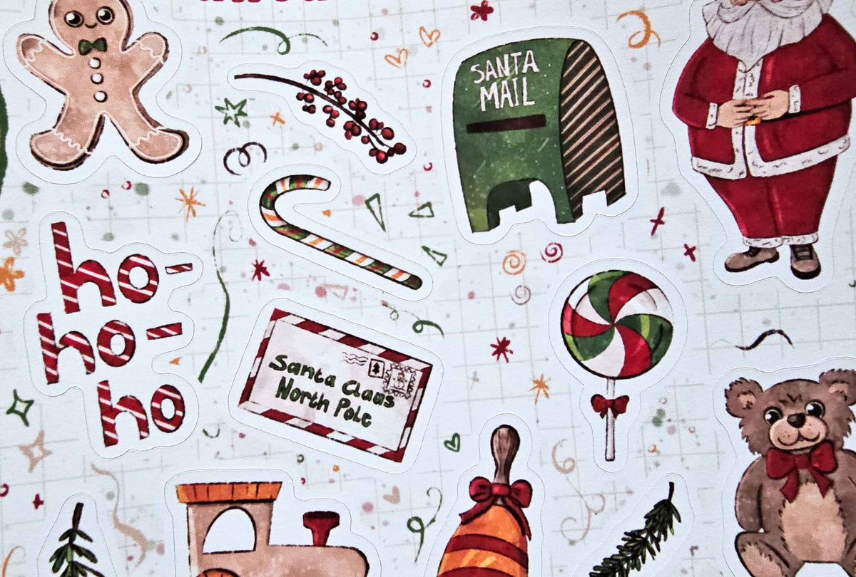 A close-up of a Christmas-themed sticker sheet featuring various illustrated holiday elements including Santa Claus, a gingerbread man, a candy cane, a green Santa mailer, a red-and-white peppermint lollipop, a Christmas ticket, a teddy bear, and 'ho ho ho' text on a white background with faint grid lines.