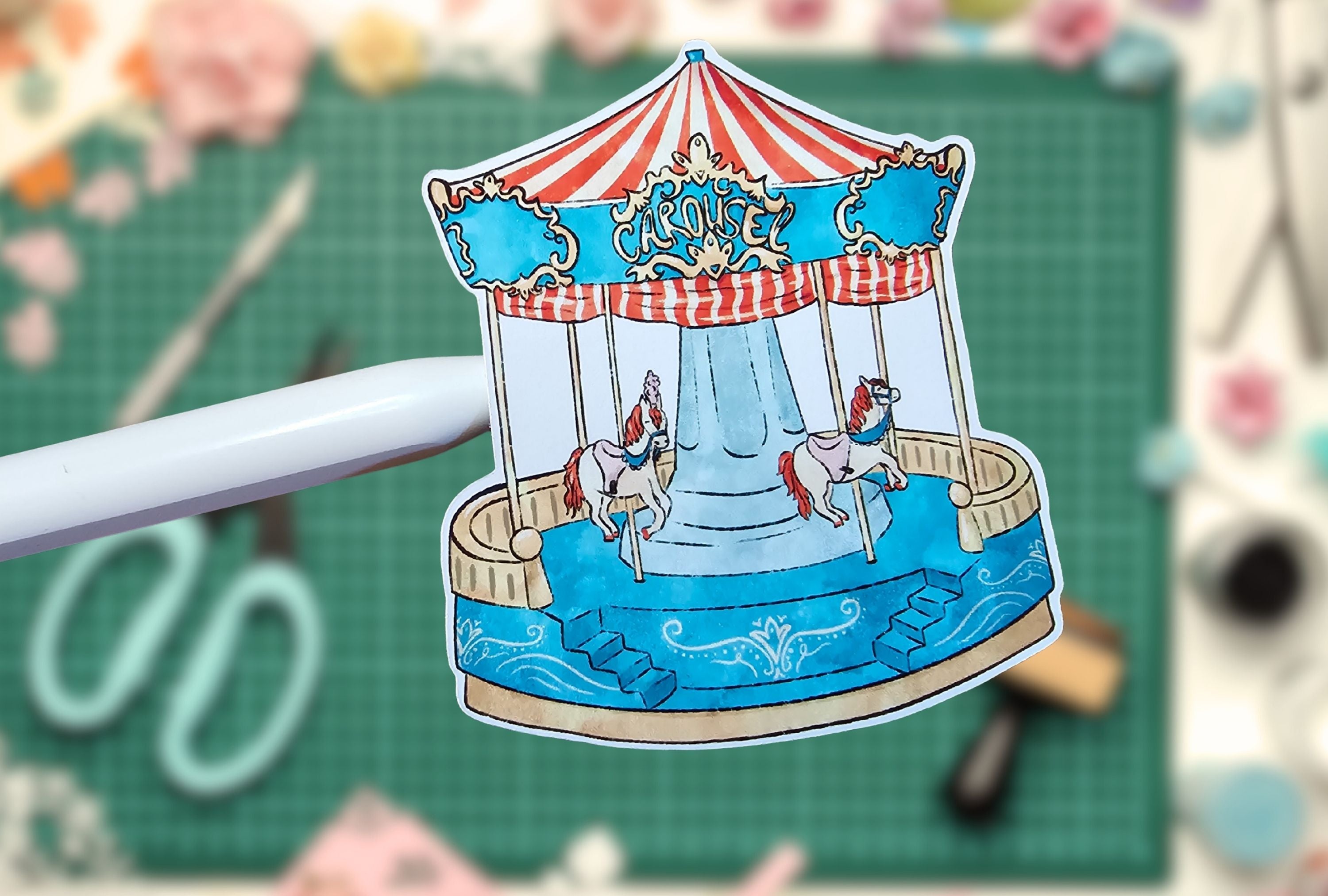 Paper cutout of a carousel with horses on a green cutting mat with scissors in the background
