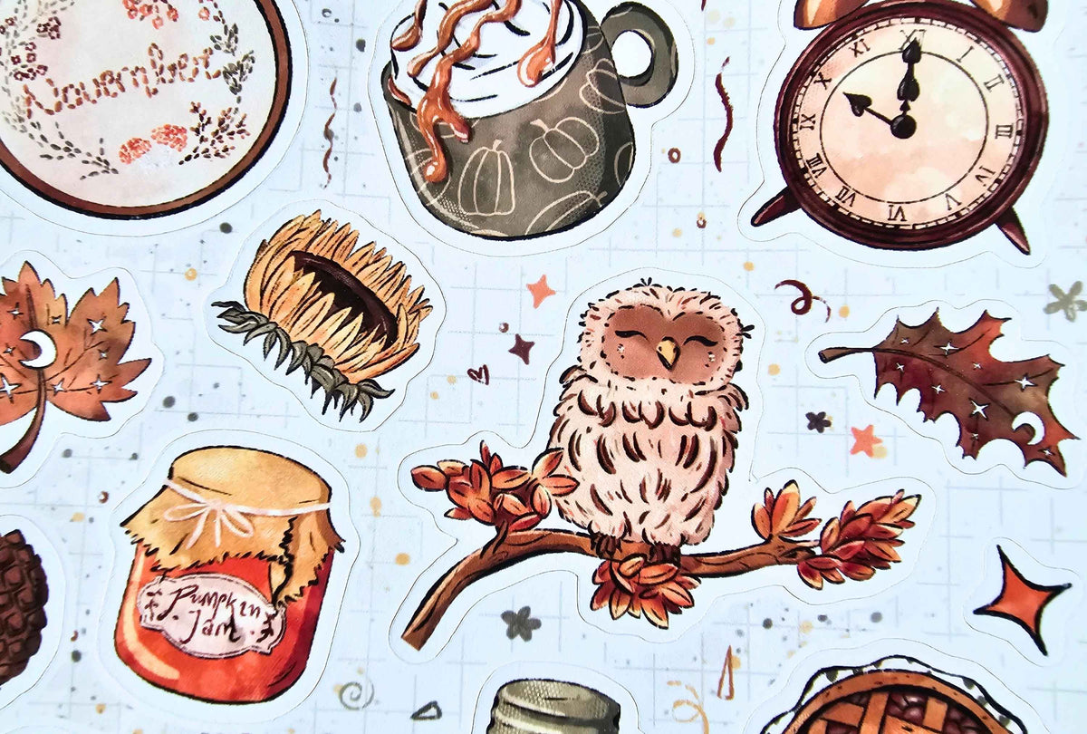 A collection of autumn-themed kiss-cut stickers arranged on a light blue grid paper background. The stickers feature illustrations of an owl on a branch with fall leaves, a pumpkin pie, a jar of pumpkin jam, a hot cocoa mug with whipped cream, a clock, a sunflower, and a maple leaf.