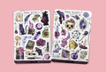Two sticker sheets titled 'Dark Rituals' on a textured surface with various creepy gothic illustrations like skulls, black cat, wtich, potions, broken mirror, forest elements, tarot cards, crystals, candles