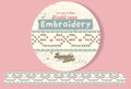 A circular product label for an embroidery washi tape roll with stiched ribbods end tiny hearts, shown on a pink background. 